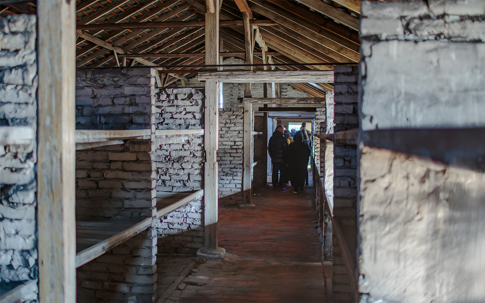 Inside Auschwitz Birkenau barracks with visitors on a guided tour.