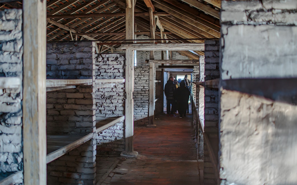 Inside Auschwitz Birkenau barracks with visitors on a guided tour.