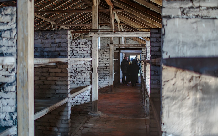 Inside Auschwitz Birkenau barracks with visitors on a guided tour.