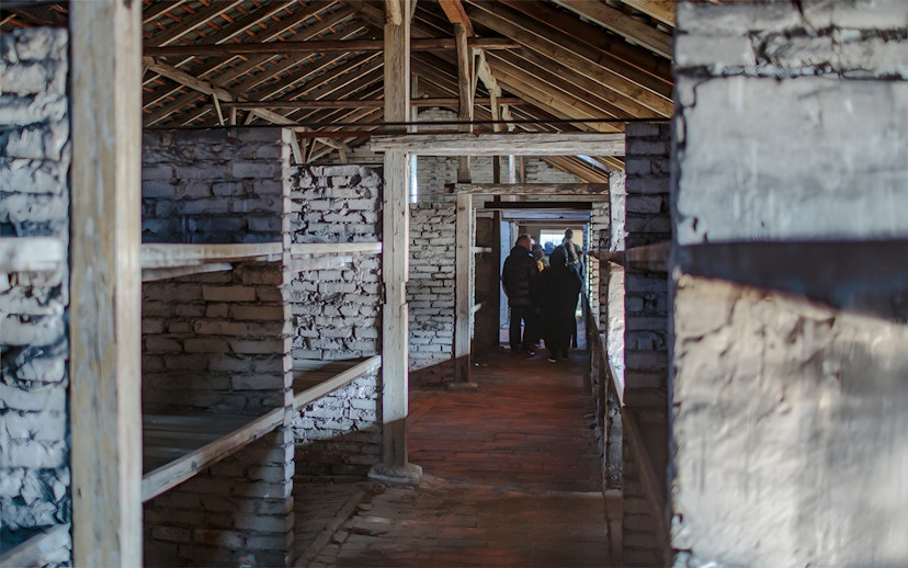 Inside Auschwitz Birkenau barracks with visitors on a guided tour.