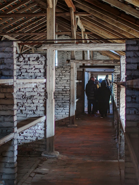Inside Auschwitz Birkenau barracks with visitors on a guided tour.