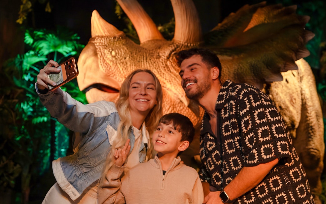 Family taking a selfie with a dinosaur exhibit at the immersive VR experience.