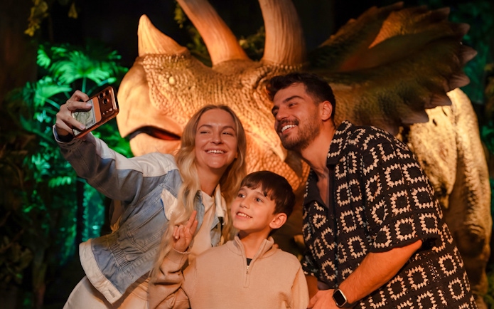 Family taking a selfie with a dinosaur exhibit at the immersive VR experience.