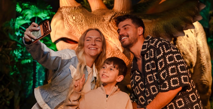 Family taking a selfie with a dinosaur exhibit at the immersive VR experience.