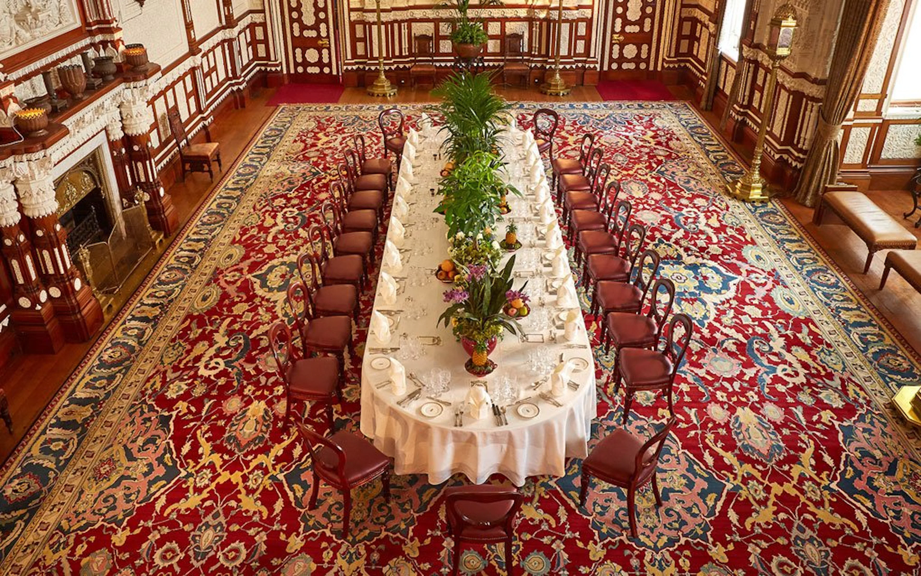 Long dining table set in the ornate Durbar Room with intricate red carpet.