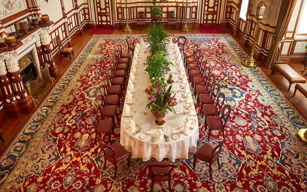 Long dining table set in the ornate Durbar Room with intricate red carpet.
