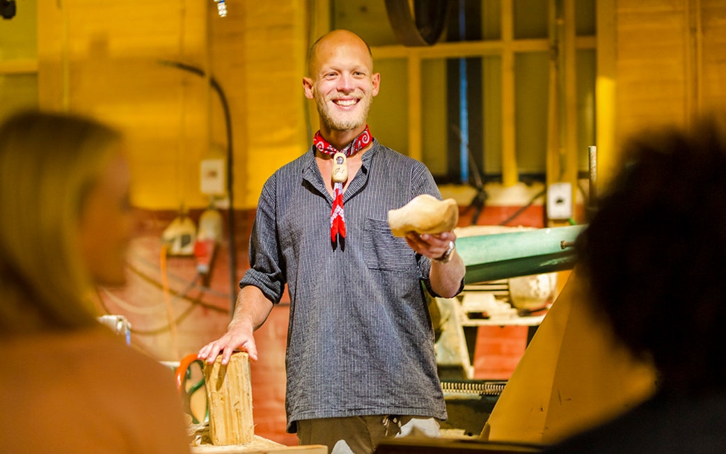 Man demonstrating wooden clog making in workshop.