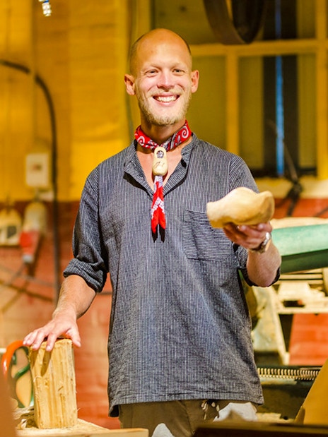 Man demonstrating wooden clog making in workshop.