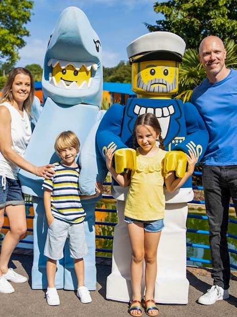 Family posing with LEGO shark and sailor figures at LEGOLAND® Windsor Resort.