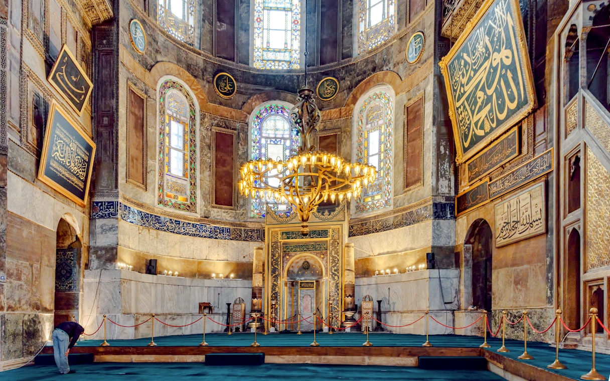 Hagia Sophia interior with ornate chandelier and Arabic calligraphy on walls.