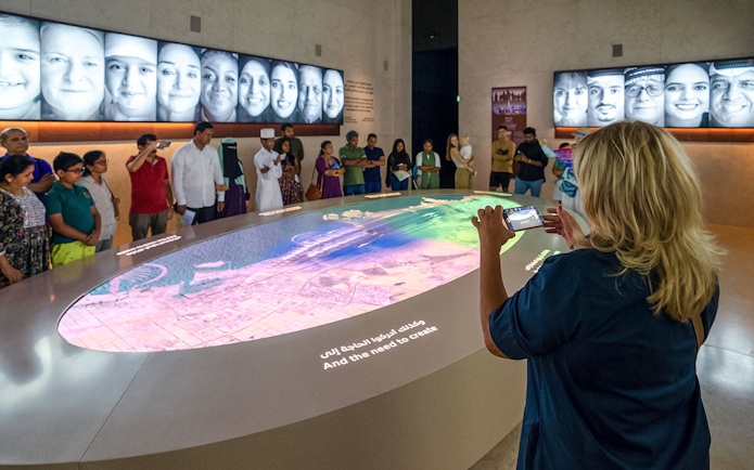 Tourist photographing interactive exhibit at Expo City Dubai with group observing.