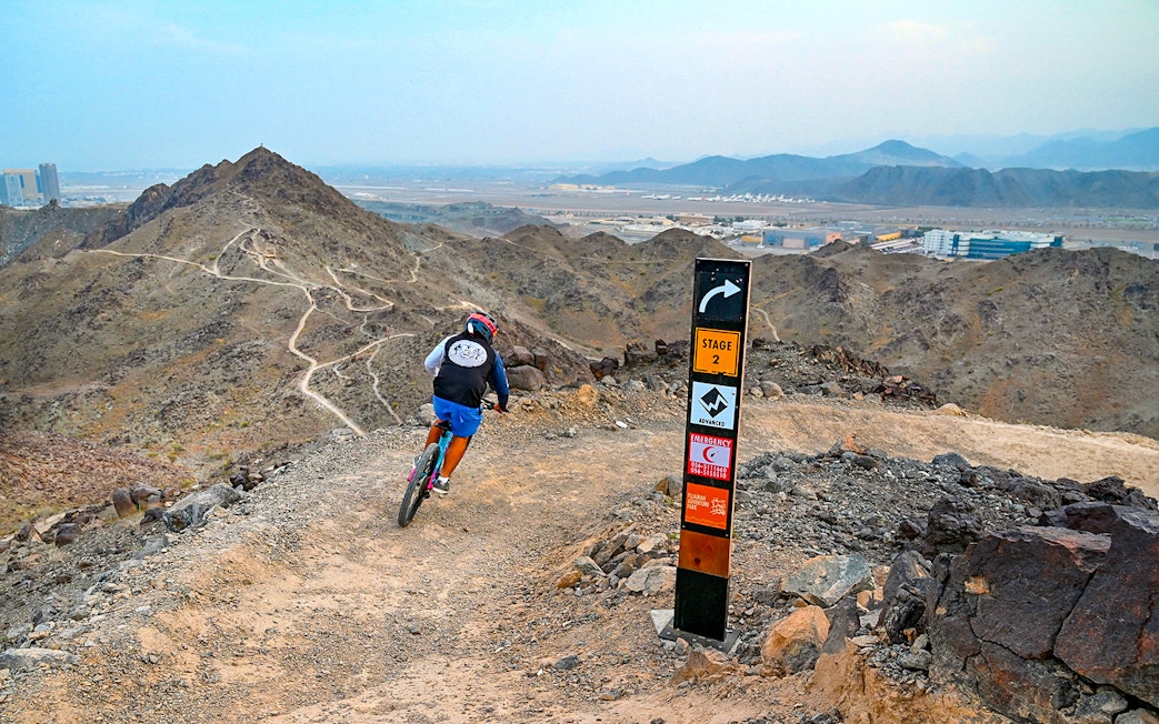Mountain biker on trail at Fujairah Adventure Park with directional sign.
