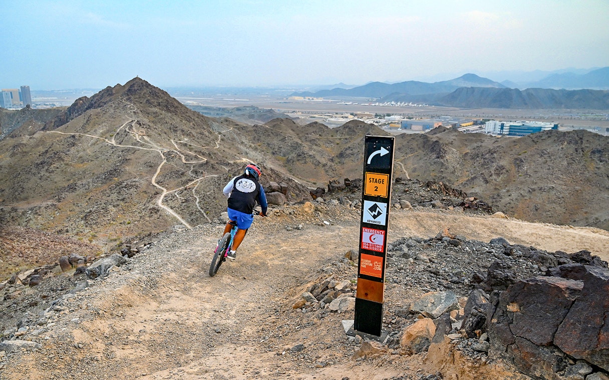 Mountain biker on trail at Fujairah Adventure Park with directional sign.