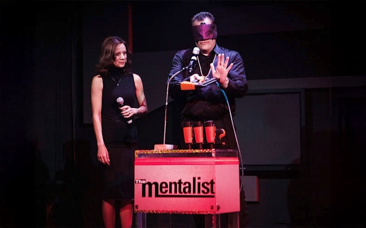 Performer on stage with blindfold, holding a microphone, during The Mentalist show.