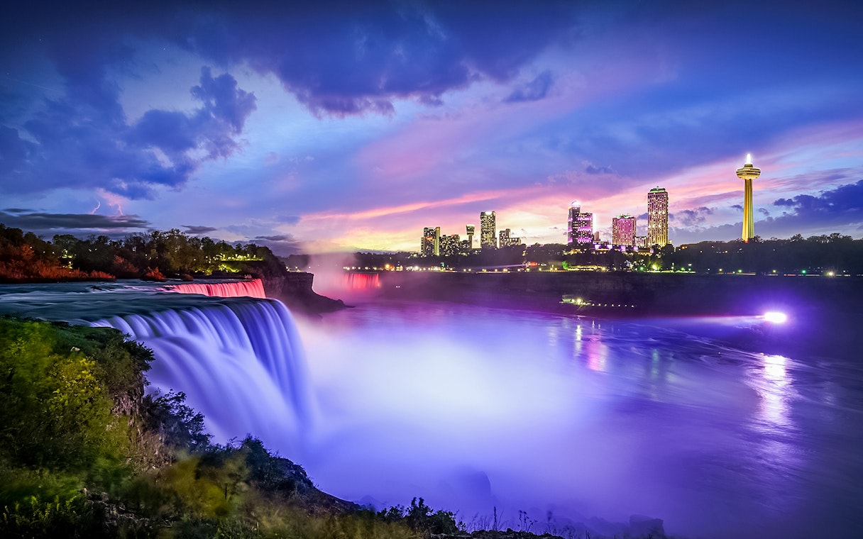 Niagara Falls illuminated at dusk with city skyline in the background, Canada.
