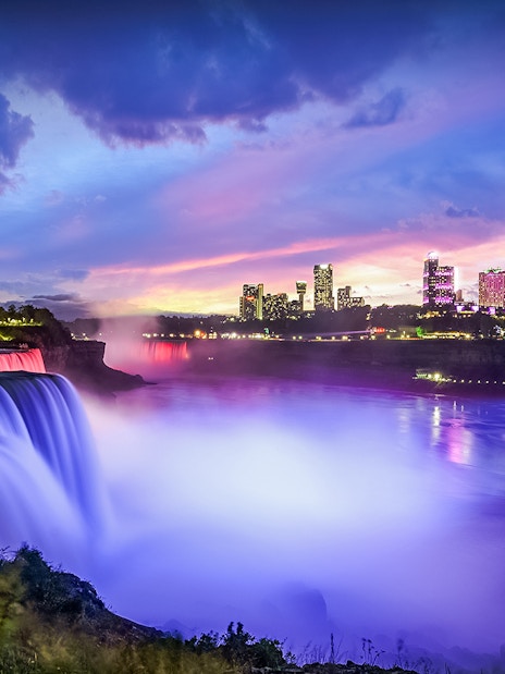 Niagara Falls illuminated at dusk with city skyline in the background, Canada.