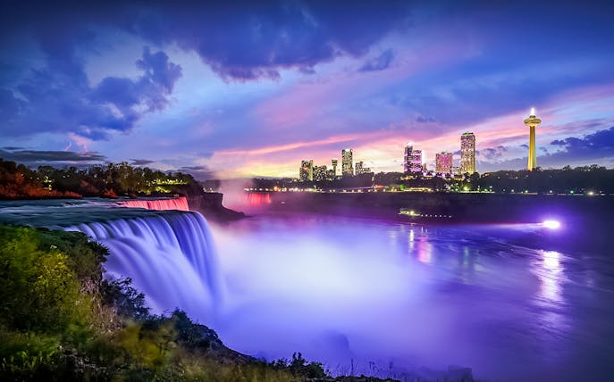 Niagara Falls illuminated at dusk with city skyline in the background, Canada.