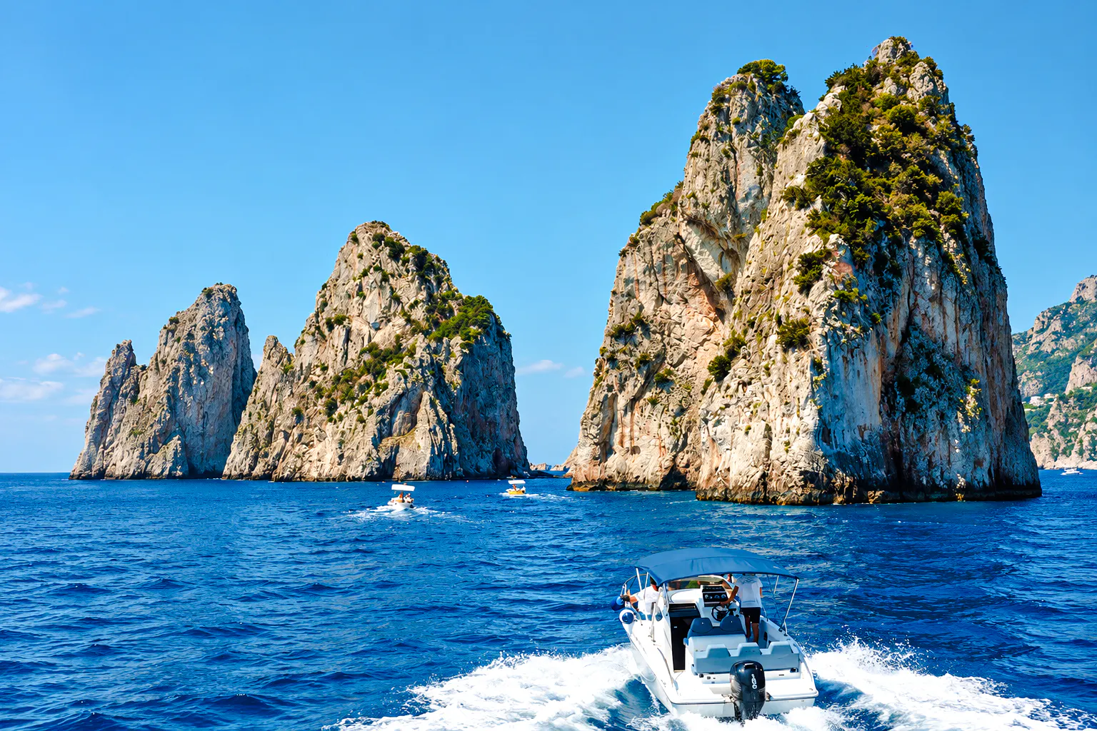 Boat approaching Faraglioni rock formations, Capri, Italy.