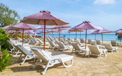 White lounge chairs under purple umbrellas on Rosario Islands beach.