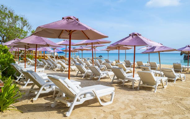 White lounge chairs under purple umbrellas on Rosario Islands beach.