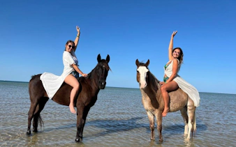 Horse riding in shallow waters at Nabq Bay with clear blue skies.
