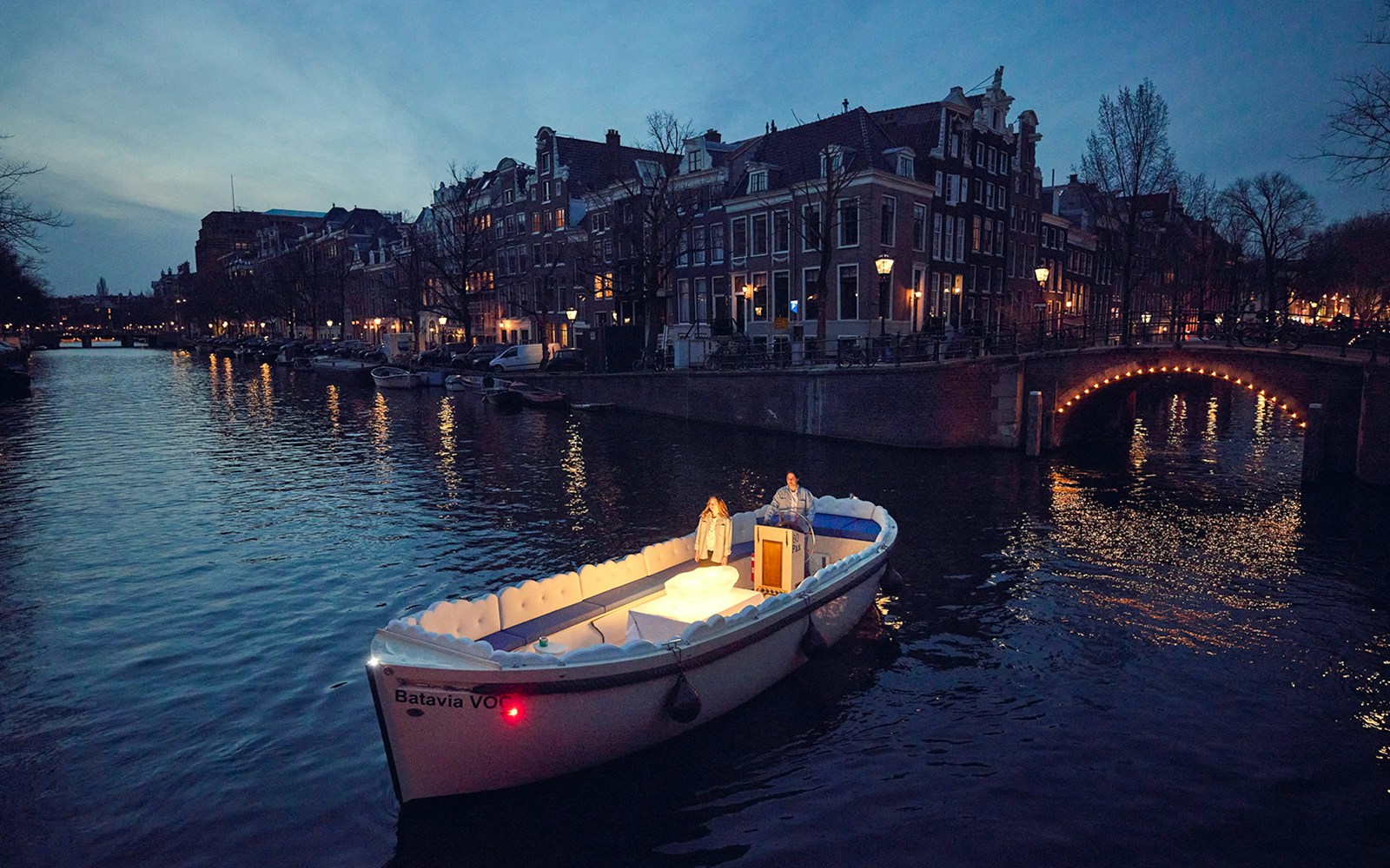 Cloud Boat Cruise on Amsterdam's canals at dusk with illuminated cityscape.