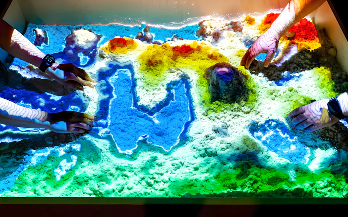 Hands interacting with colorful sand display at DeJa Vu Museum Berlin.