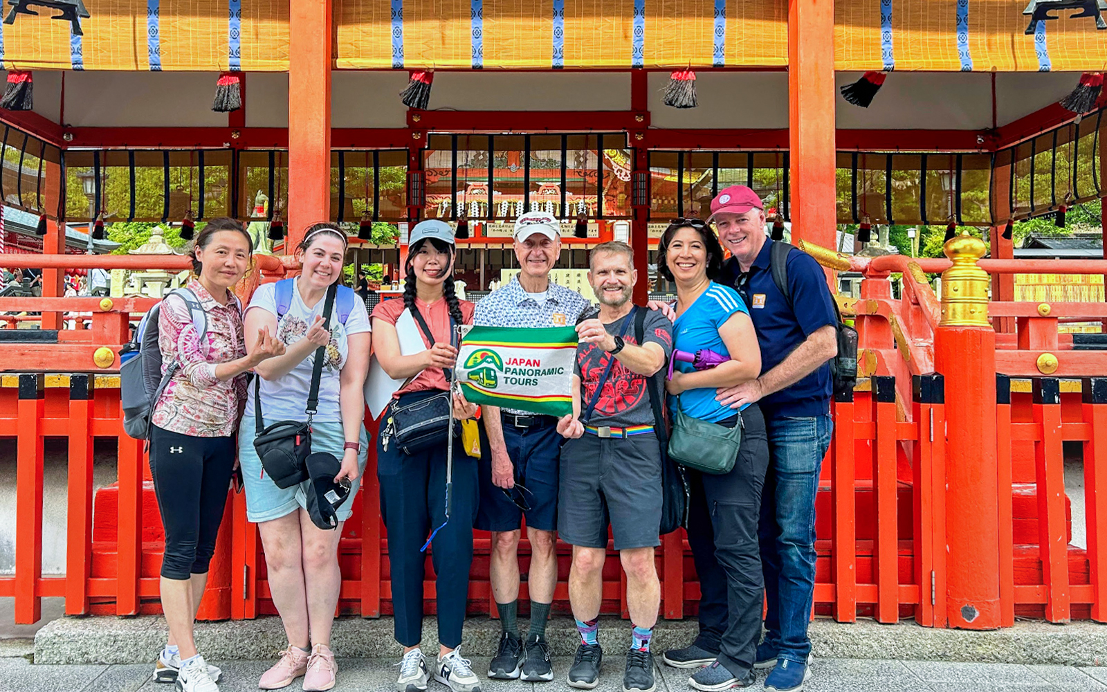 Group of tourists holding a tour sign in front of a traditional Kyoto shrine.