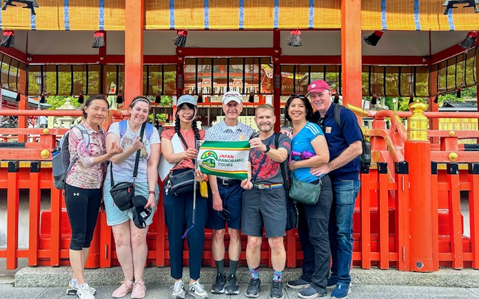 Group of tourists holding a tour sign in front of a traditional Kyoto shrine.