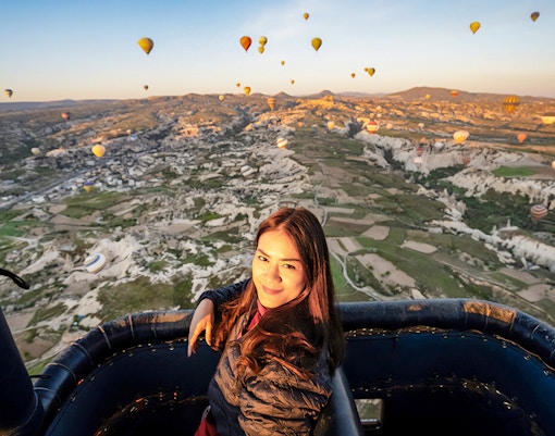 Woman in hot air balloon basket over Cappadocia's Göreme at sunrise.