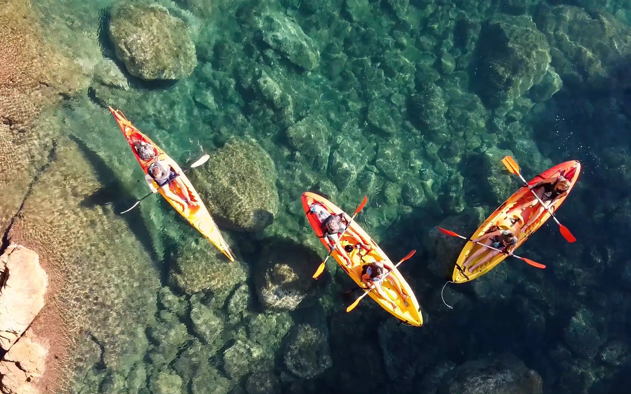 Visitors kayaking over clear waters at Costa Brava, Spain.