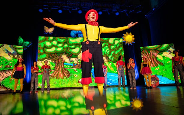 Performers on stage in colorful costumes during Cantajuegos 20 Años show with vibrant backdrop.