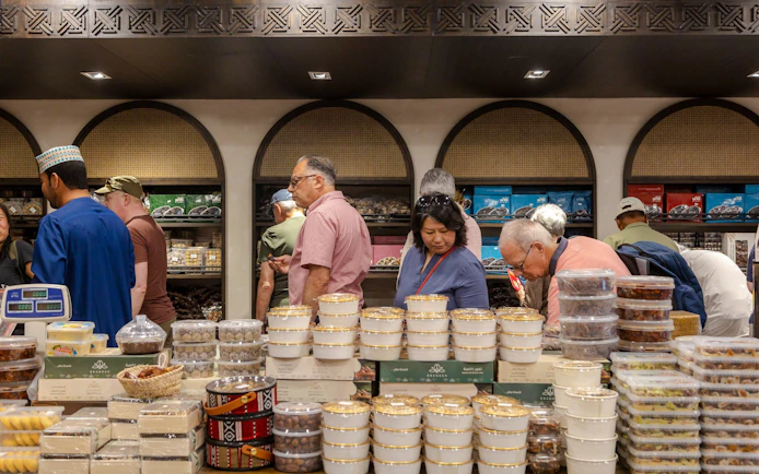Tourists exploring a market with traditional Omani sweets during Nizwa and Oman Grand Canyon Tour.