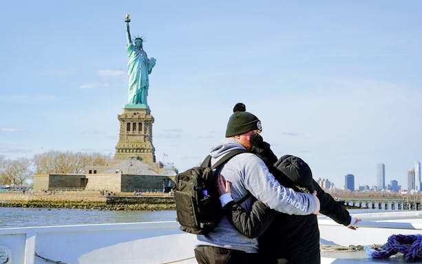 Couple embracing on a cruise with the Statue of Liberty in the background, New York City.