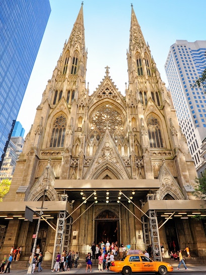 St. Patrick's Cathedral facade with visitors and a yellow taxi in New York City.