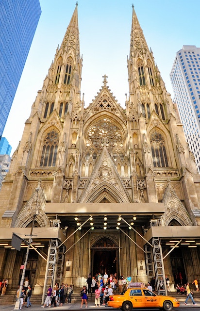 St. Patrick's Cathedral facade with visitors and a yellow taxi in New York City.