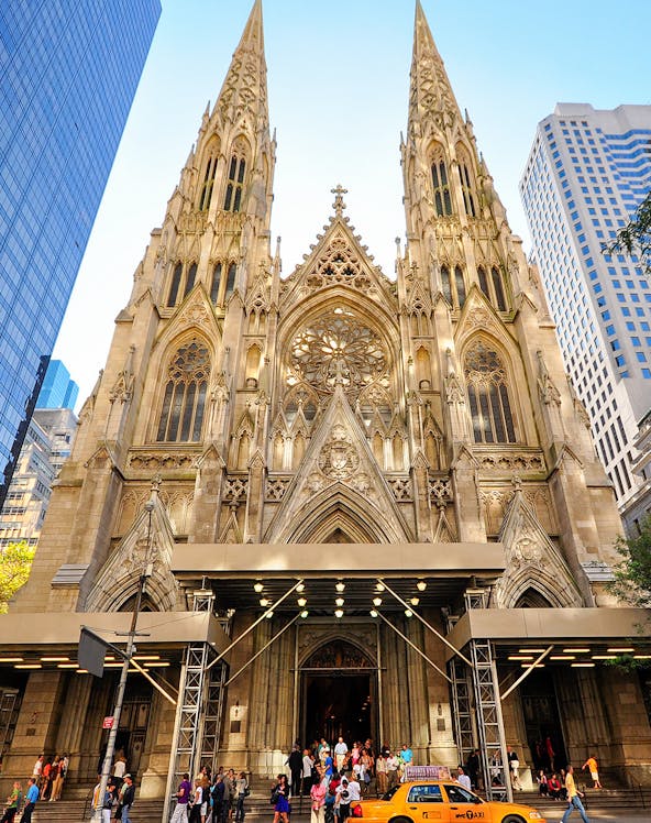 St. Patrick's Cathedral facade with visitors and a yellow taxi in New York City.