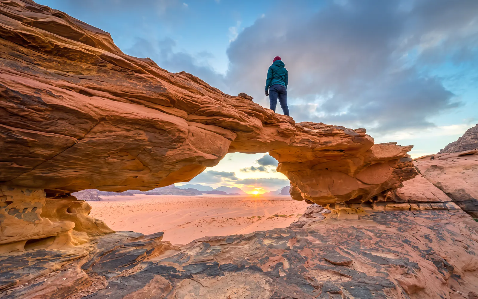 Person standing on rock arch at sunset in Wadi Rum desert, Jordan.