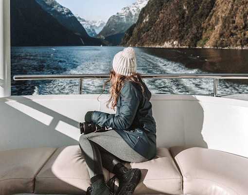 Cruise passenger enjoying Milford Sound's mountain views and lush greenery, Queenstown day trip.