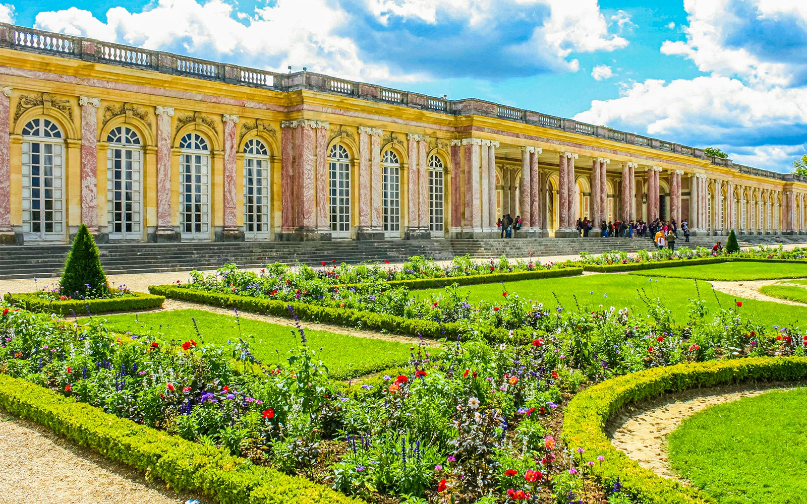 Grand Trianon palace exterior with pink marble columns and manicured gardens in Versailles, France.