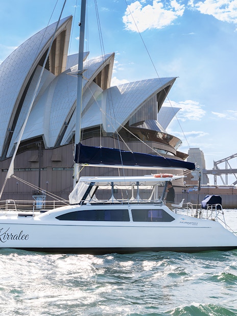 Catamaran Kirralee cruising near Sydney Opera House and Harbour Bridge during Vivid Sydney.