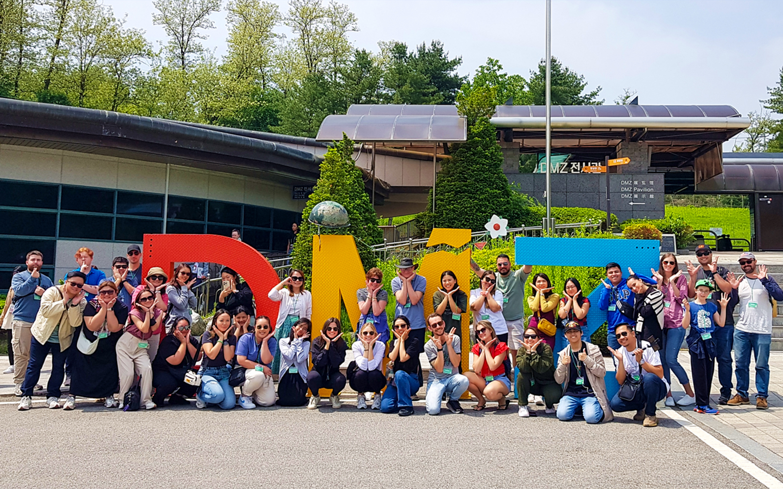 Tour group posing in front of colorful DMZ sign, South Korea.