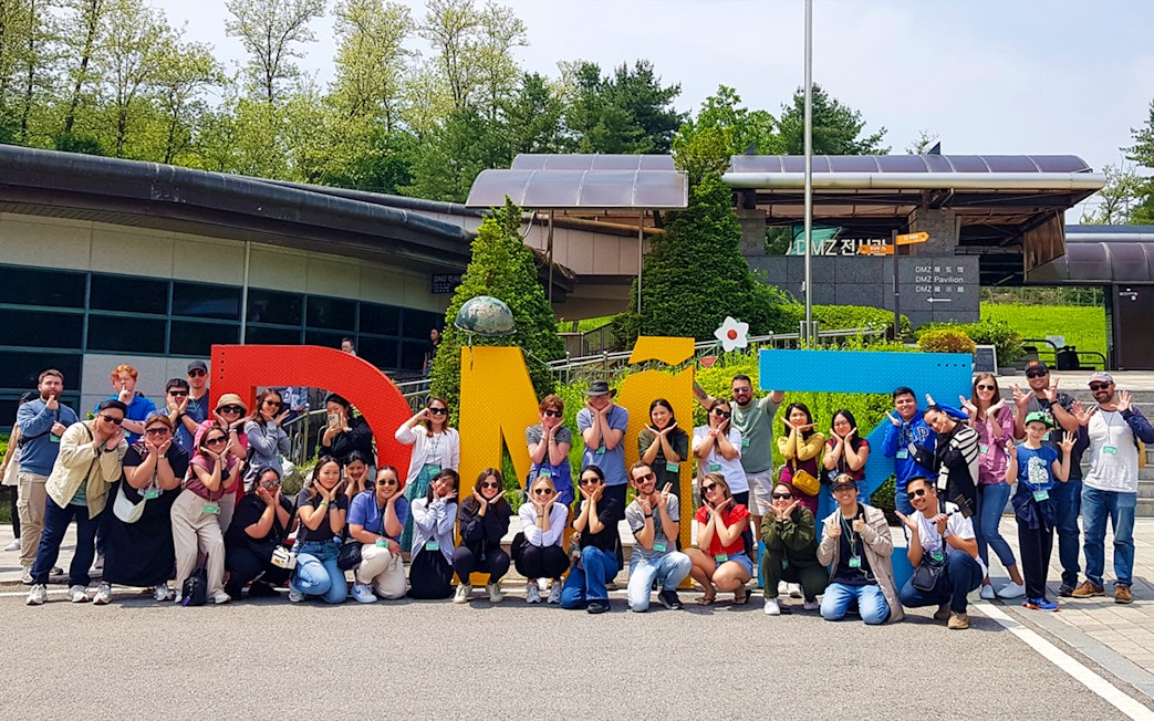 Tour group posing in front of colorful DMZ sign, South Korea.
