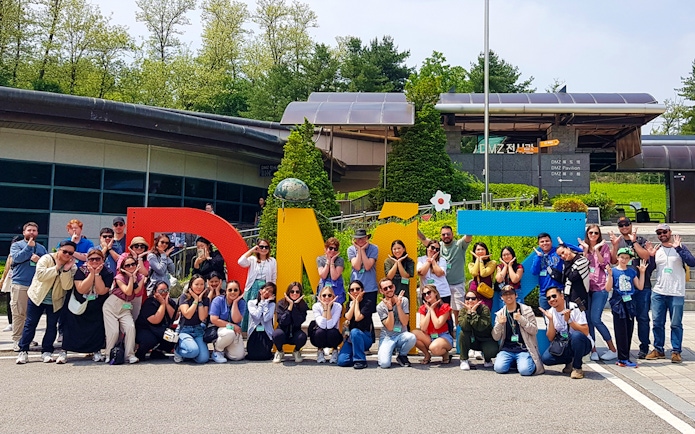 Tour group posing in front of colorful DMZ sign, South Korea.