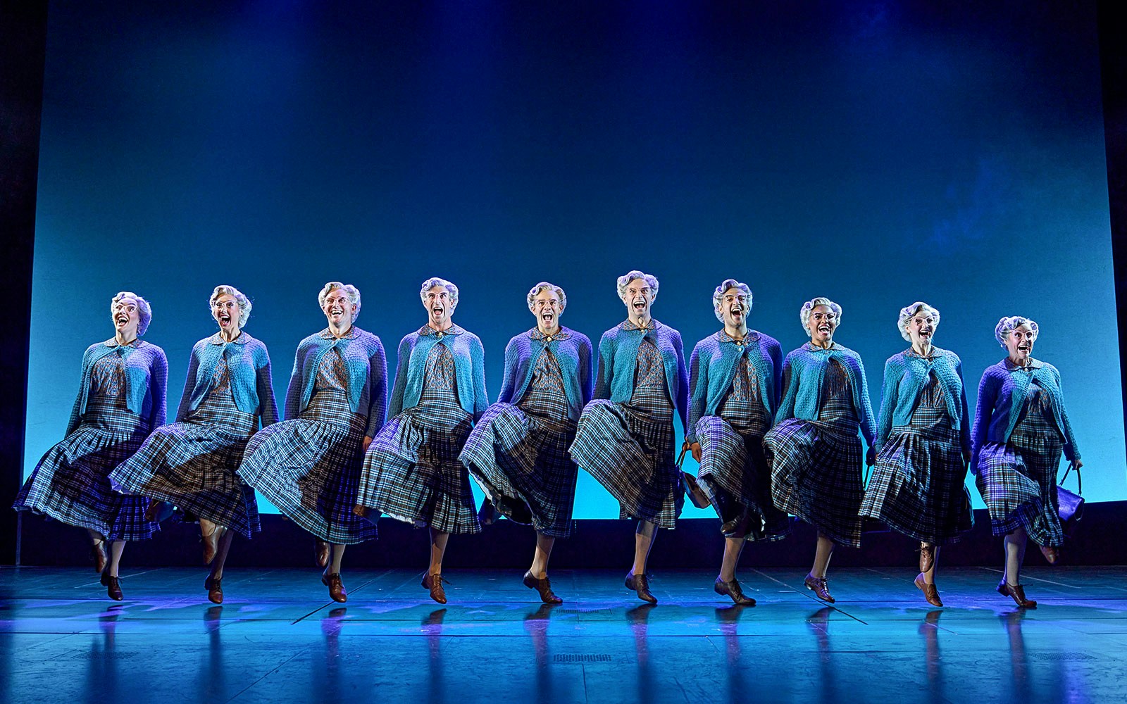Performers in Mrs. Doubtfire musical dancing in coordinated plaid costumes on stage.