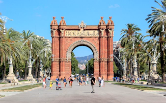 Arc de Triomf in Barcelona with people walking and palm trees lining the path.