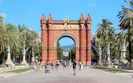 Arc de Triomf in Barcelona with people walking and palm trees lining the path.