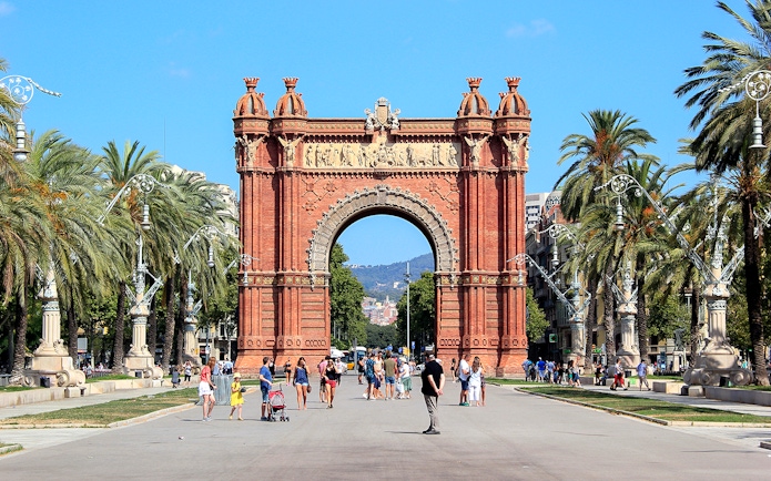 Arc de Triomf in Barcelona with people walking and palm trees lining the path.