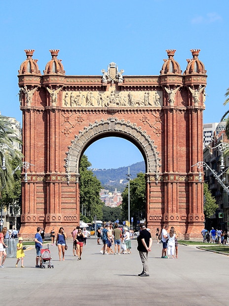 Arc de Triomf in Barcelona with people walking and palm trees lining the path.