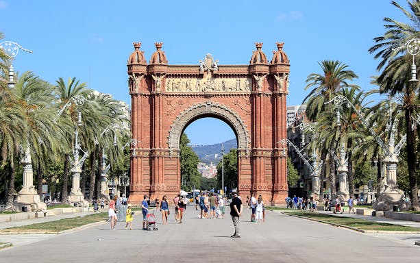 Arc de Triomf in Barcelona with people walking and palm trees lining the path.